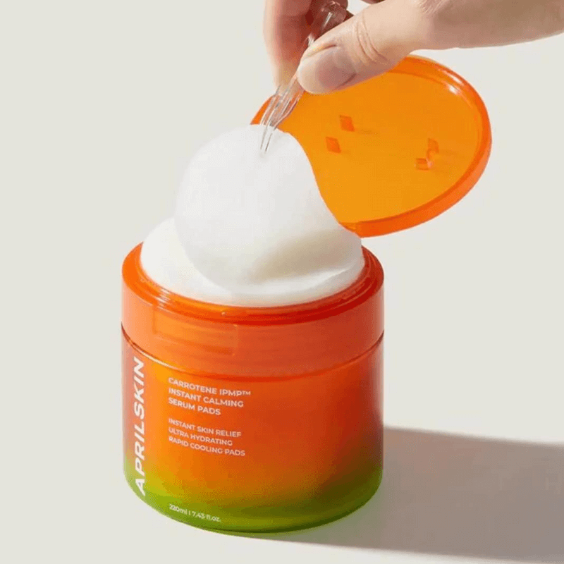APRILSKIN Carrotene IPMP Instant Calming Serum Pads in a jar with a hand holding a dropper.