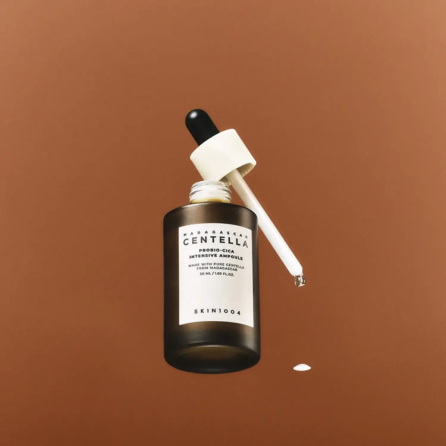 Skin1004 Madagascar Centella Probio-Cica Intensive Ampoule 50ml in dark glass bottle with dropper on brown background.