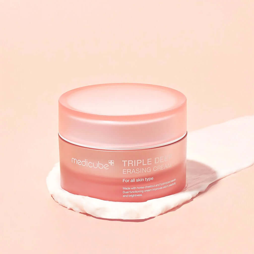 Medicube Triple Deep Erasing Cream in a pink jar on a soft surface, suitable for all skin types, promoting brightness and hydration.