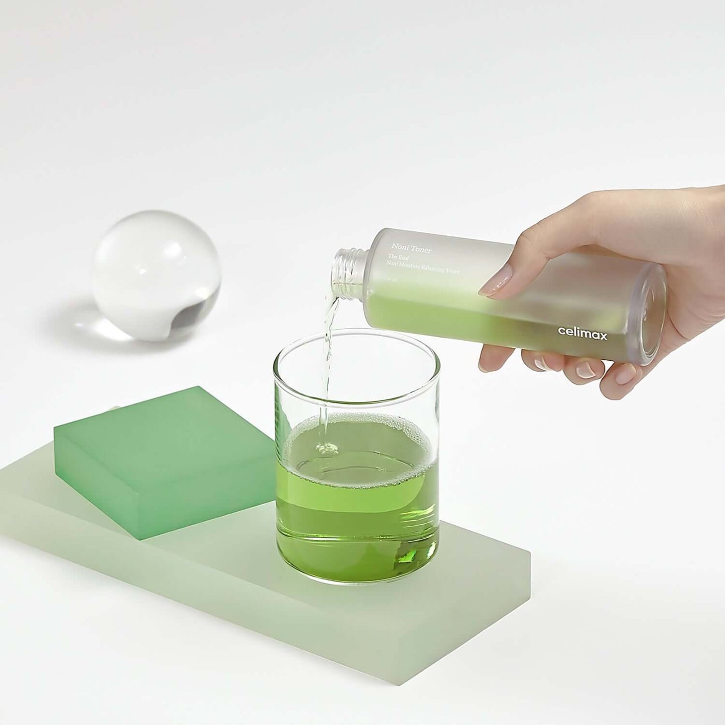 Celimax Noni Moisture Balancing Toner being poured into a glass, showcasing its refreshing green liquid.