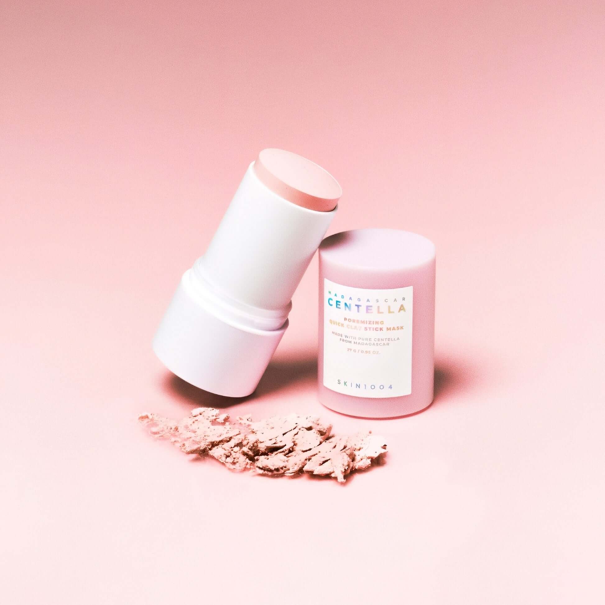 Skin1004 Madagascar Centella Poremizing Quick Clay Stick Mask on a pink background with clay powder.
